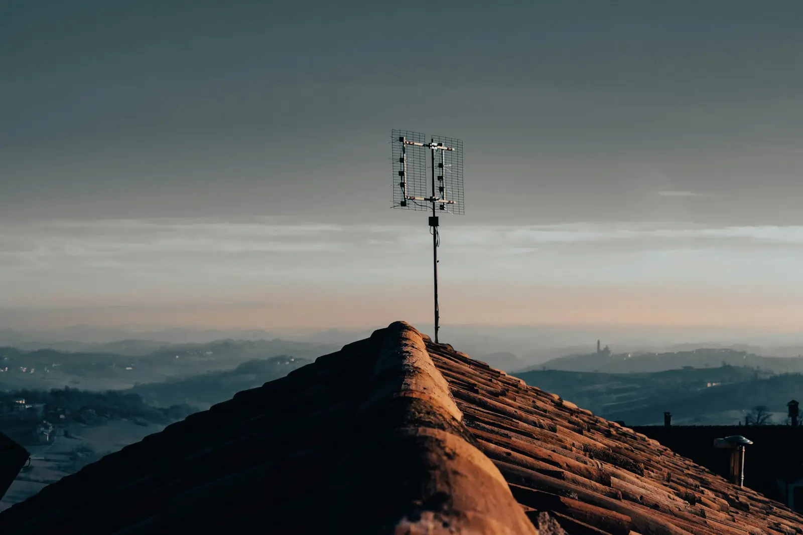 Un mât d’antenne planté sur une crête au crépuscule, les collines s’effaçant dans la brume.