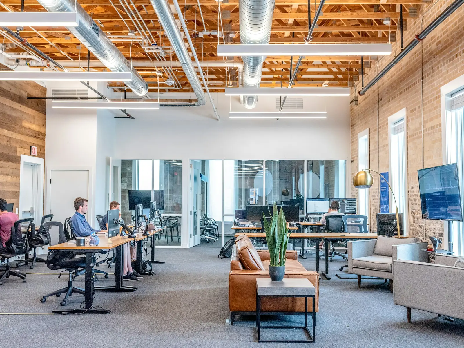 Un plateau de bureaux ouvert sous une charpente de bois : des postes de travail, des canapés bas et de grandes fenêtres.