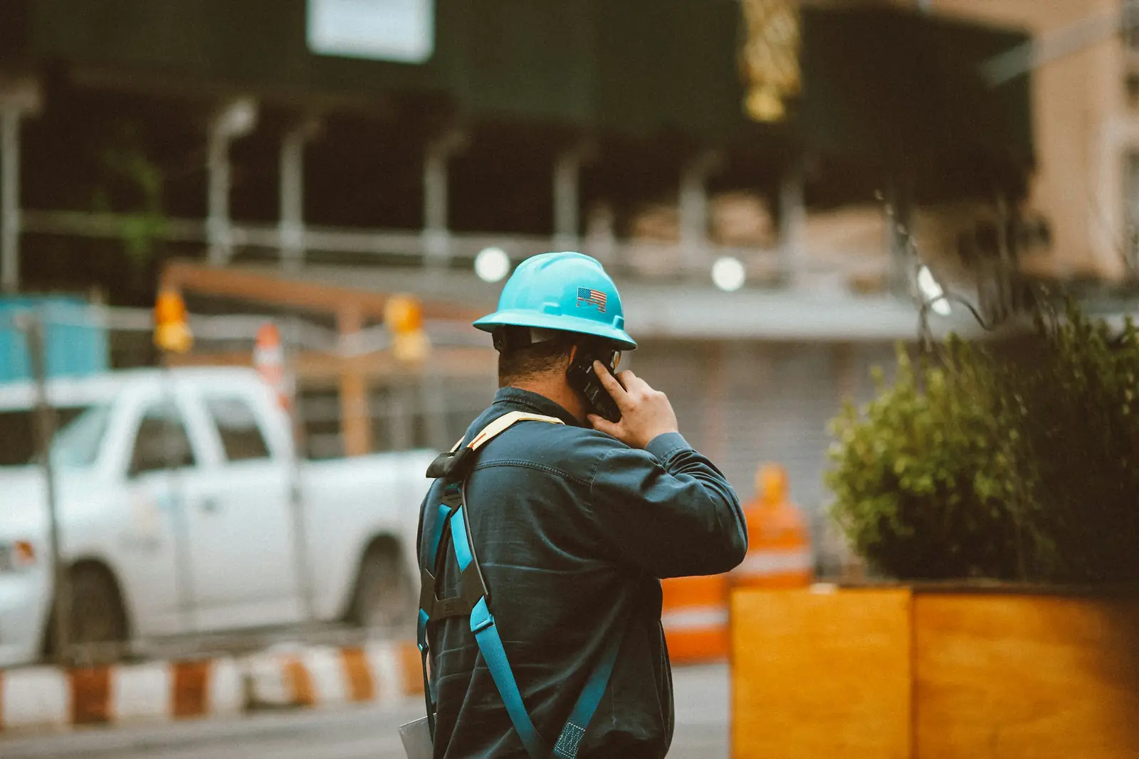 Une personne en casque de chantier au téléphone, au bord d’une voie, la circulation floue derrière.