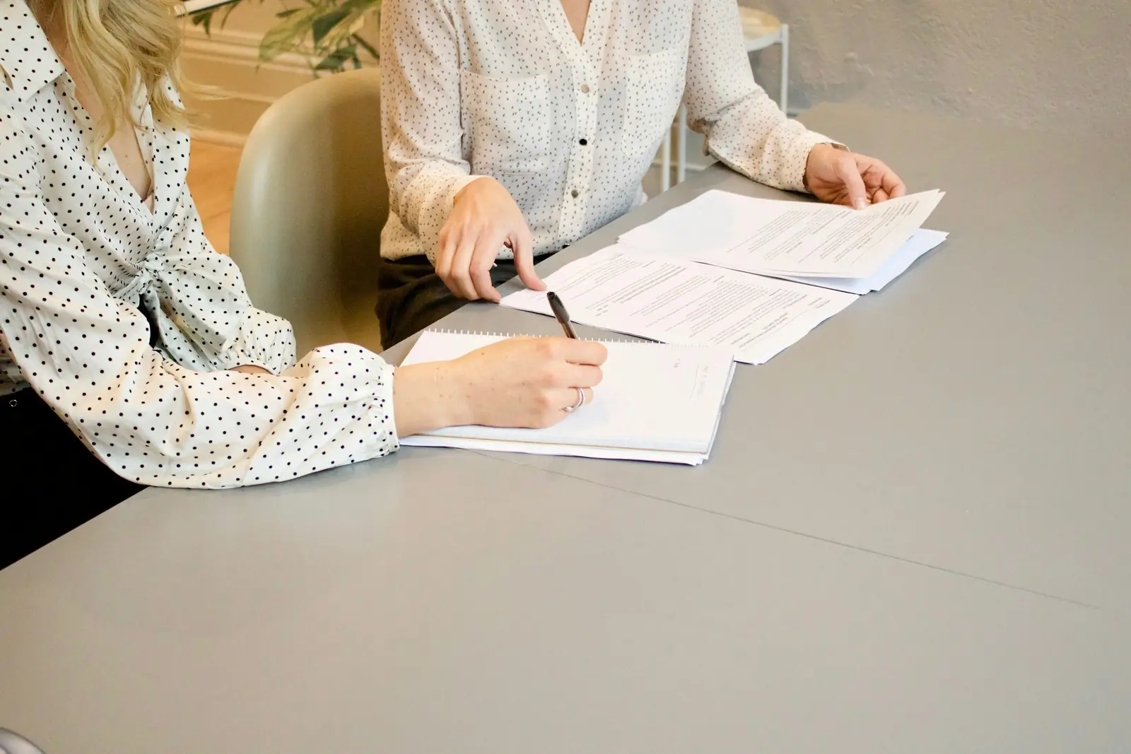 Deux personnes assises à une table, l’une remplissant un formulaire au stylo, des papiers étalés devant elles.