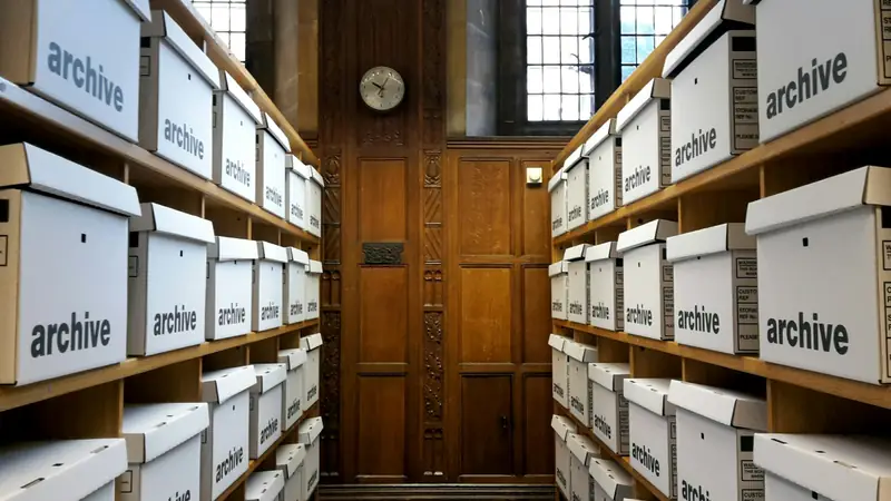 Une salle d’archives, boîtes alignées sur des étagères de bois.