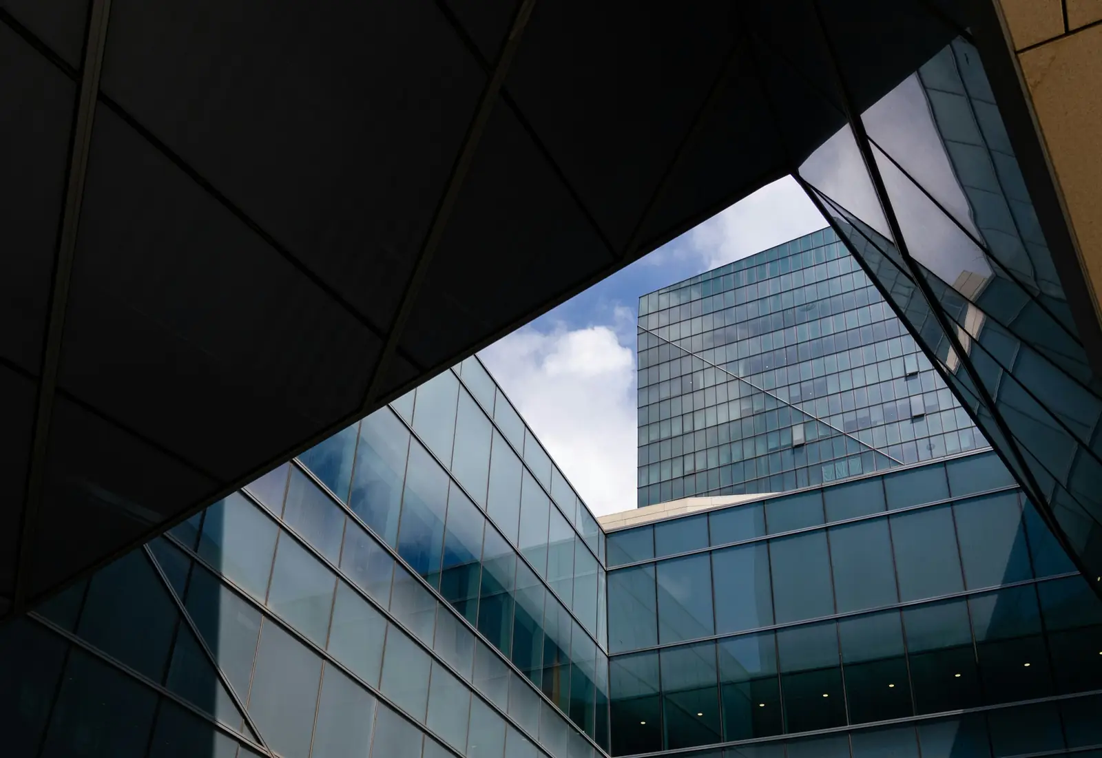 Une façade de verre vue depuis le dessous d’un auvent sombre, le ciel et l’immeuble se reflétant dans les vitres.