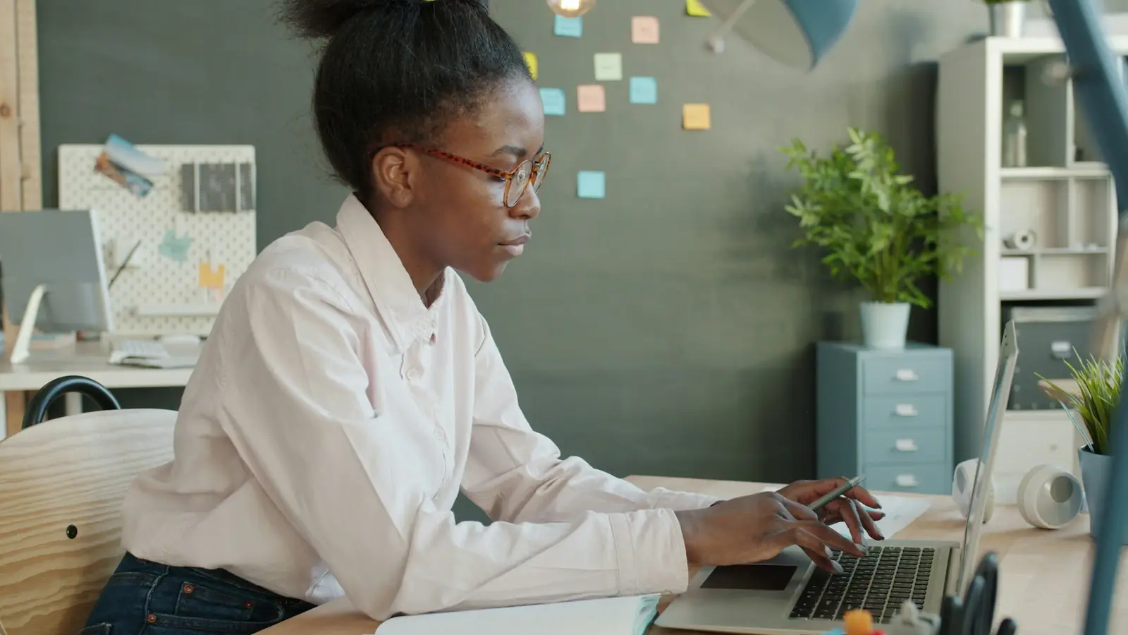 Une personne à son bureau devant un ordinateur portable, un mur de pense-bêtes colorés derrière elle.