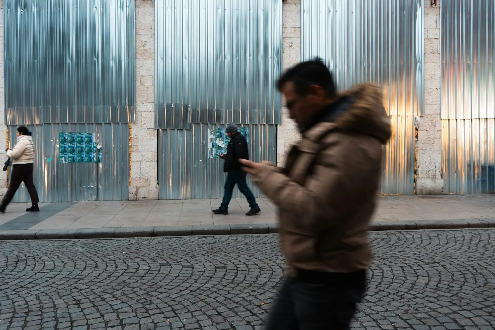Une personne marche le long d’un mur de tôle ondulée en regardant son téléphone.