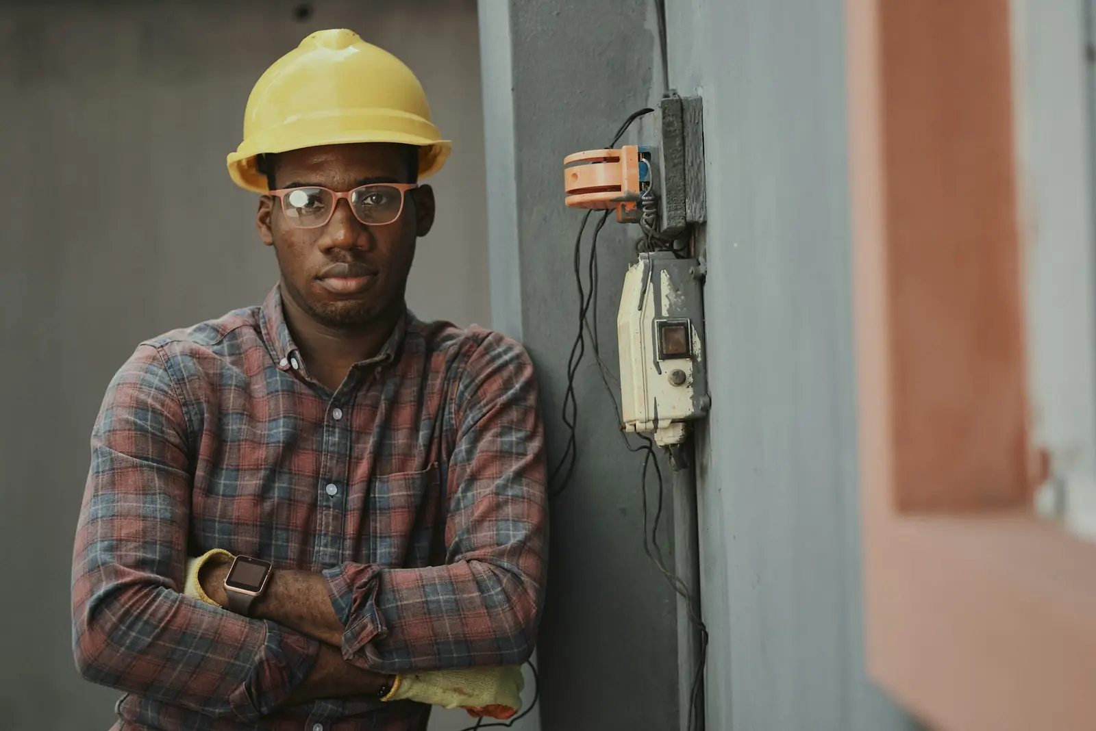 Une personne en casque de chantier debout à côté d’un téléphone mural, dans un couloir de béton.