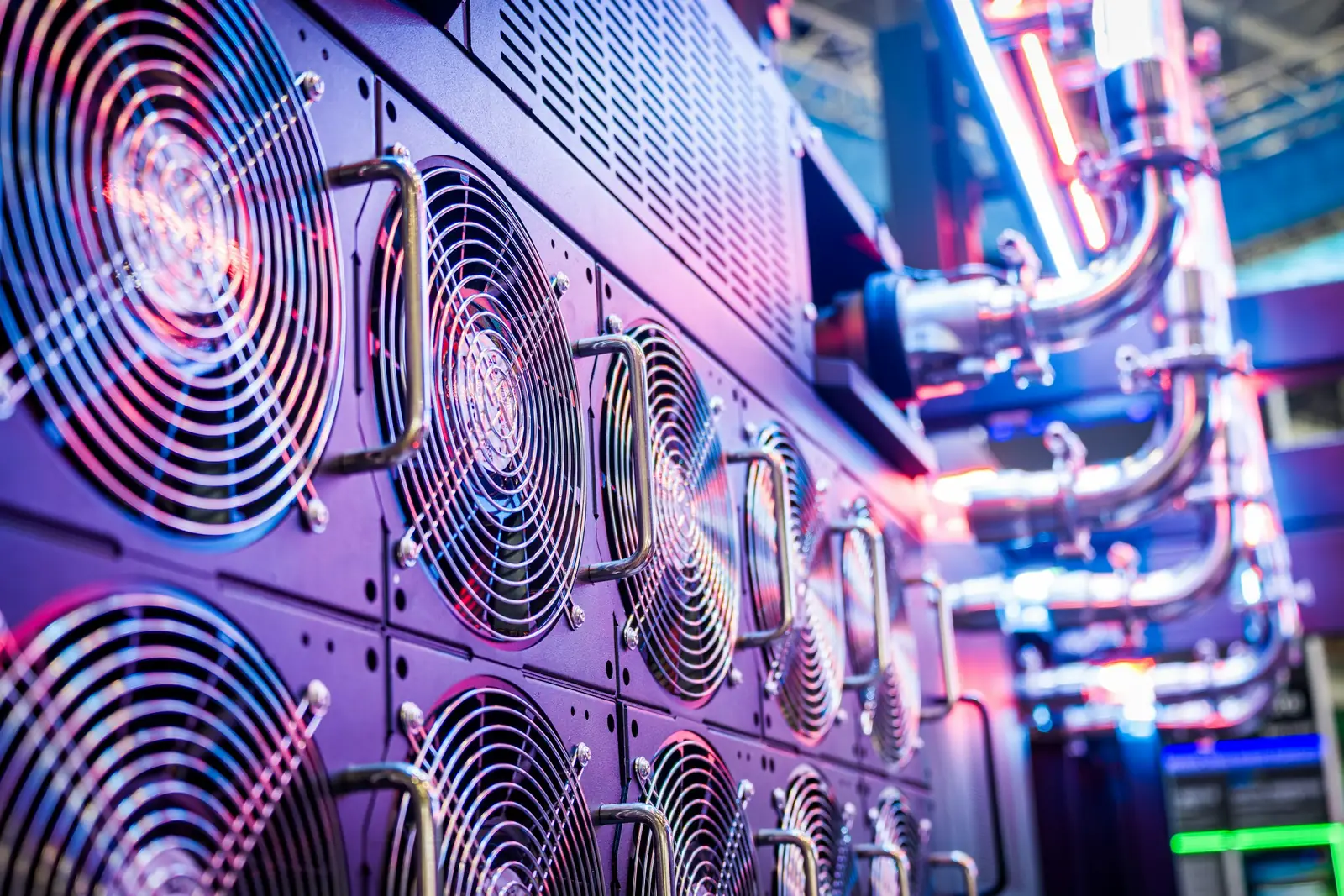 Un mur de ventilateurs et de tuyauteries dans une salle machine, éclairé en bleu et violet.